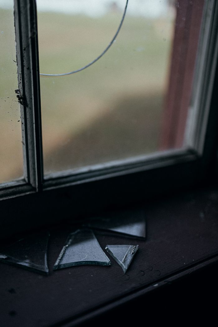 Dark and moody shot of a window with broken glass and scattered shards on the sill.