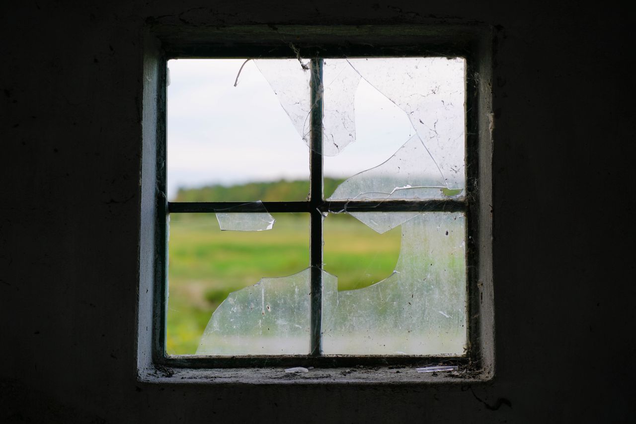 Close-up of a broken window with a green landscape visible through the glass.